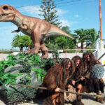 dinosaurio con 3 personas disfrazadas de cromañón