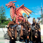 dragón rojo acompañado de 3 guardianes del dragón con disfraces medievales y portando hachas