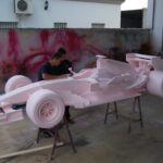trabajadores comprobando detalles de la escultura de un coche de carreras