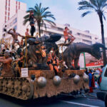 carroza de cabeza gigante de bestias con personas encima bailando